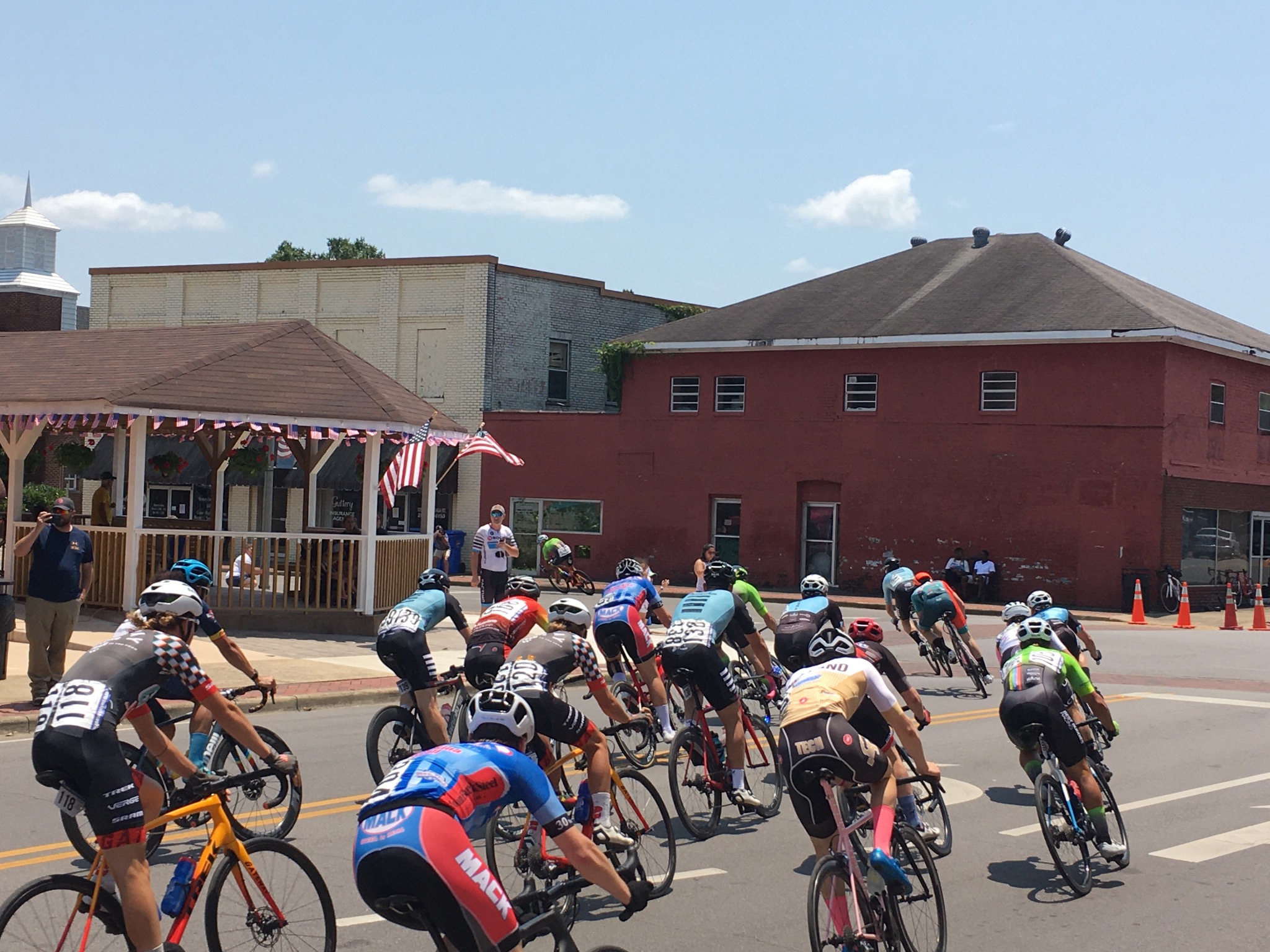 Cyclists racing through downtown Piedmont past the gazebo and brick buildings.